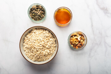 Ingredients for healthy homemade granola with Gluten Free Rolled oats or porridge oats, variety of chopped nuts and seeds, and maple syrup. Preparation for cooking at home. Marble background