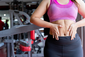 Fat woman holding excessive fat belly lower back, overweight fatty belly at fitness gym. Diet lifestyle, weight loss, stomach muscle, healthy concept.