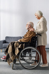 side view of senior woman touching shoulder of handicapped husband, sick on dementia