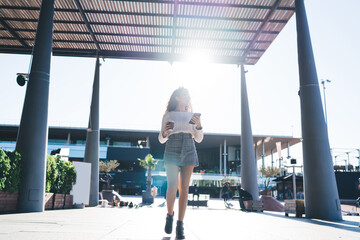 Anonymous young lady walking on sidewalk with smartphone