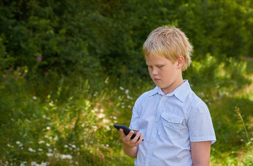 A boy in a white shirt holds a phone in his hand