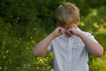 A boy rubs his eyes with both hands on a walk in the Park