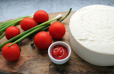 Homemade cheese made from goat's milk, small tomatoes on a branch, red sauce lie on a wooden Board on a wooden background. The concept of cooking delicious and healthy food