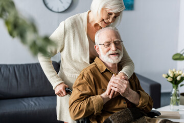 selective focus of smiling woman embracing happy, disabled husband