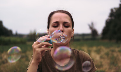 The girl blows soap bubbles. A young woman sits in nature and blows soap balls. The person in front.