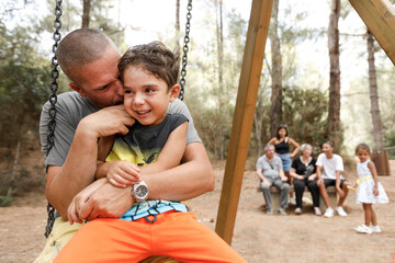 Bambino gioca con il suo pap√† bianco nel seduti nell'altalena di un parco - sullo sfondo il...