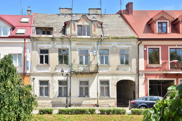 Old destroyed tenement house with broken windows among new houses.