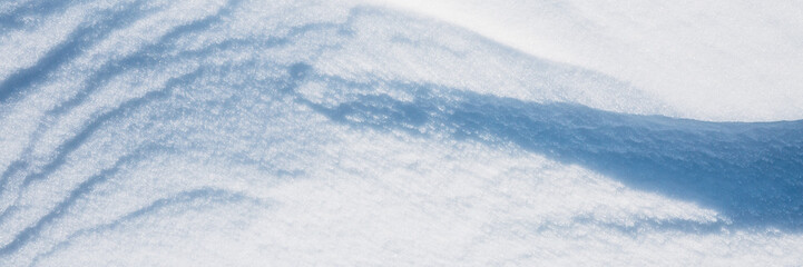 Beautiful winter background with snowy ground. Natural snow texture. Wind sculpted patterns on snow surface. Wide panoramic texture for background and design.