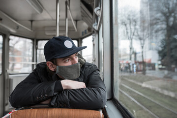 Male wearing face mask inside public transport watches at the window with rainy weather
