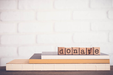 The word DONATE, alphabets on wooden rubber stamps on top of books with bricks background, blank copy space, vintage minimal style. Concepts of give, aid, help, share and charity.