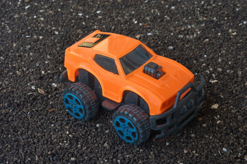 Fototapeta na wymiar Plastic orange 4x4 car toy on dirt ground, mini suv vehicle