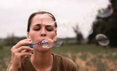 The girl blows soap bubbles. A young woman sits in nature and blows soap balls. The person in front.