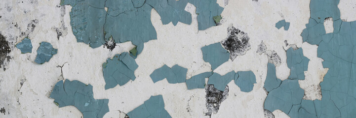 Peeling paint on the wall. Panorama of a concrete wall with old cracked flaking paint. Weathered rough painted surface with patterns of cracks and peeling. Wide panoramic grunge texture for background