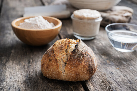 Homemade sourdough bread bun next to ingredients - flour, water and starter yeast