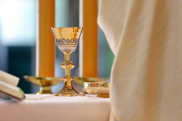 Chalice on the altar and priest celebrating mass in the background