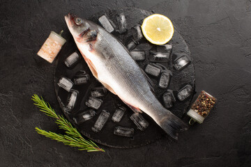 Fresh sea bass with ice cubes,rosemary,lemon,sea salt and dried pepper on black background.Top view.