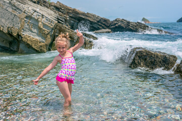 A little girl in a bright pink swimsuit poses and enjoys in the backwaters of the coastal waves. A girl is resting on the Glass Bay in the city of Vladivostok