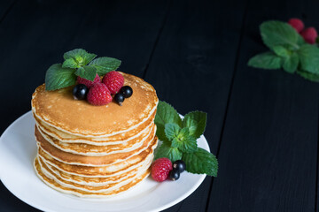 American classic pancakes with raspberry, black currant and mint on dark wooden background, selective focus, copy spase.