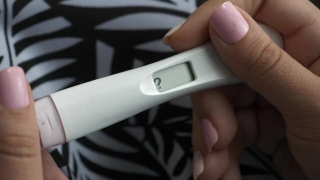 Woman holding a digital pregnancy test in her hands that is showing a question mark. Closeup shot of the test unit being held in her hands.
