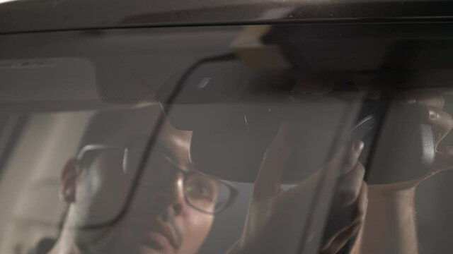 Man installing a dashcam inside a car on the front windshield to film everything that is happening while driving.