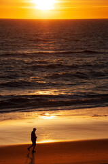 A jogger is running along the beach with the reflection of a sunrise on the ocean.