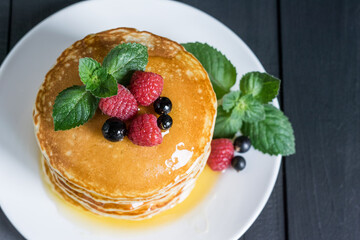 American classic pancakes with raspberry, black currant, honey and mint on dark wooden background, selective focus.