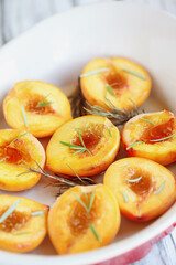 Naklejka na ściany i meble Fresh homemade roasted peaches baked in brown sugar and fresh rosemary sprigs. Selective focus with blurred foreground and background.