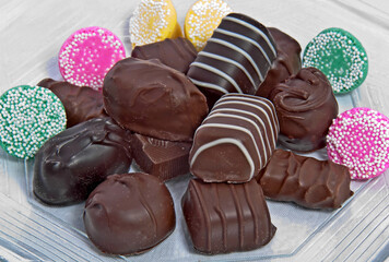 This is a closeup plate of gourmet chocolate squares and pastel mint candies on a light background.  Horizontal with no people in this sweet image.