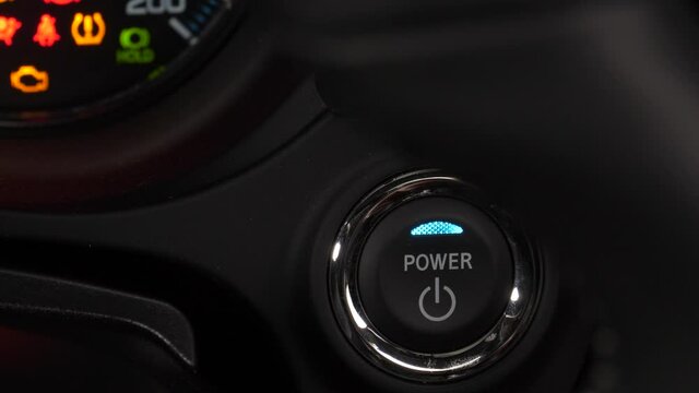 Closeup of a finger pushing the button to start a car. Power button being switched ON.
