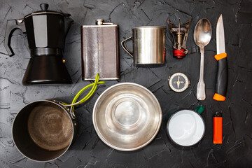 Kitchen accessories in the campsite. Cauldron, geyser coffee maker, spoon, knife, cup, flask, lighter.