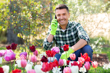 gardening and people concept - happy smiling middle-aged man with flowers calling on smartphone at summer garden