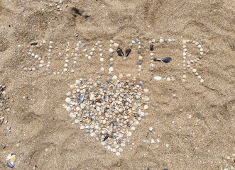 A large heart of seashells laid out on sea sand with the inscription and letters summer. Photography, concept, top view.