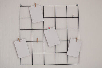 Black metal grid mood inspiration board with mockup empty notes on clamps on a simple white wallpaper background for ideas, organizations, memories, wishlists and photos with  copy space on them.