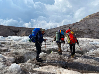 Three climbers with backpacks stand on a snowy ice mountain trail.