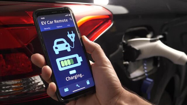 Mobile phone showing the charging status of an EV vehicle being charged in the background.