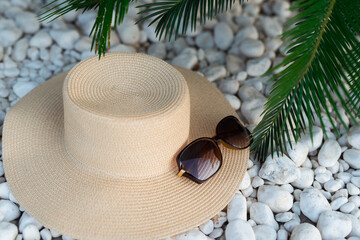 straw hut, sunglasses and palm tree leaves on the pebble beach, vacations concept.