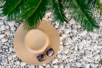 straw hut, sunglasses and palm tree leaves on the pebble beach, vacations concept.