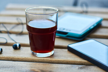 Wooden table with glass of black strong coffee and mobile headphones, smartphone and e-book. Work and study in cafe.