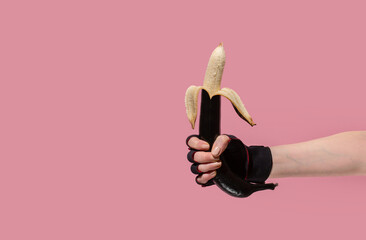 Hands holding a painted black banana on a pastel background. Concept for sex shops, adult toys - obrazy, fototapety, plakaty