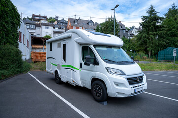 modern motorhome stands on a pitch made of concrete underground in front of a half-timbered town