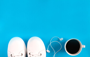 Sports flat lay with coffee, white sneakers and earphones on blue background. Fitness concept. Concept healthy lifestyle. Top view. Copy space.