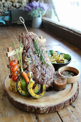 Plank steak and grilled vegetables on wooden table.