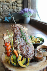 Plank steak and grilled vegetables on wooden table.