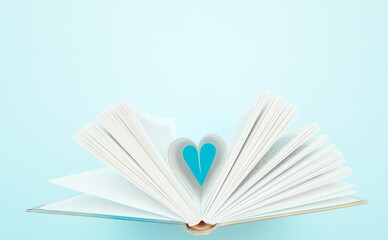 Pages of book curved into a heart shape on blue backdrop. Flat lay, empty space for text....