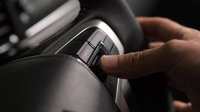 Driver of a vehicle using the switch and buttons of the car steering wheel to adjust settings while driving on the road.