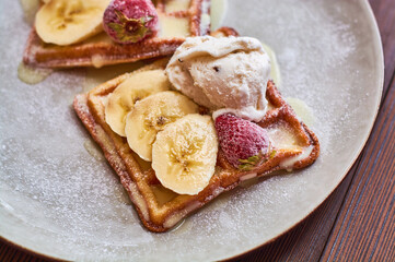 Large gray ceramic plate with fresh Belgian sweet waffles, ice cream, strawberries, bananas and condensed milk. Delicious breakfast and dessert.