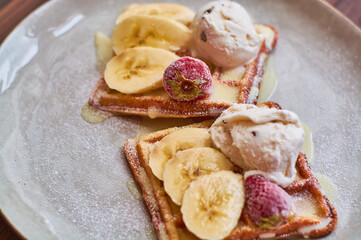 Large gray ceramic plate with fresh Belgian sweet waffles, ice cream, strawberries, bananas and condensed milk. Delicious breakfast and dessert.