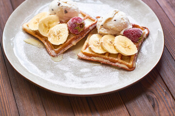 Large gray ceramic plate with fresh Belgian sweet waffles, ice cream, strawberries, bananas and condensed milk. Delicious breakfast and dessert.
