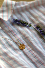 Striped pastel blouse, gold necklace with vintage pendant and lavender flower. Selective focus.
