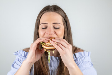 Portrait of a beautiful young woman eating a burger, isolated on white background